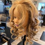 Mannequin with long, voluminous curls prepped by apprentice Chloe, ready to be styled into an updo.