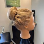 Mannequin head showing the right side of a Chignon updo with loose, textured twists created by apprentice Chloe.