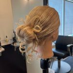 Mannequin head styled in a voluminous textured bun updo by apprentice Chloe during Week 8 training.