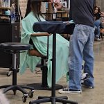 Stylist performing a precision horizontal hair cut on a model with long dark hair at a professional education seminar.