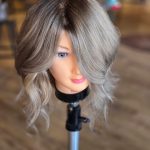 A mannequin head with a styled, wavy bob featuring a seamless melt from dark roots to ashy, cool-toned blonde highlights.